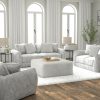 Upholstered sofa set with matching loveseat, armchair, and fluffy ottoman in a bright, modern living room with wood floors and white curtains.